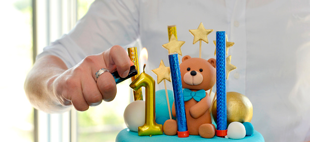 father lights the candle on a son birthday cake.