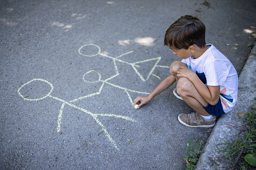 Overhead shot of little boy drawing a picture of his family and feeling sad