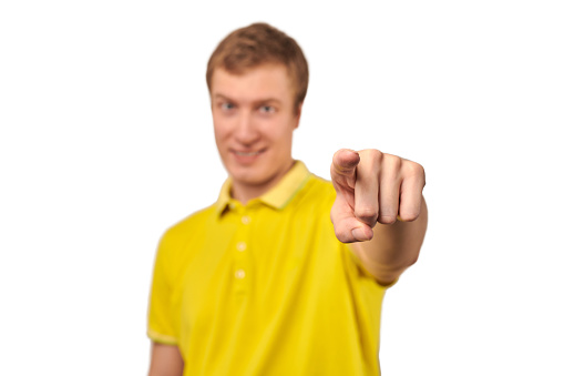 Smiling attractive guy in casual yellow T-shirt pointing finger forward isolated on white background. Funny young handsome man pointing forward, indicates goal, guy pointing at camera