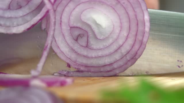 Macro shot hands cut red onion into rings on cutting board. Cooking food.