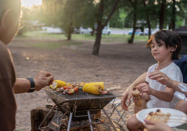 Happy Asian family having barbecue together. Cooking grilled bbq for dinner during camping on summer beach. Happy Asian family having barbecue together. Cooking grilled bbq for dinner during camping on summer beach. family bbq beach stock pictures, royalty-free photos & images