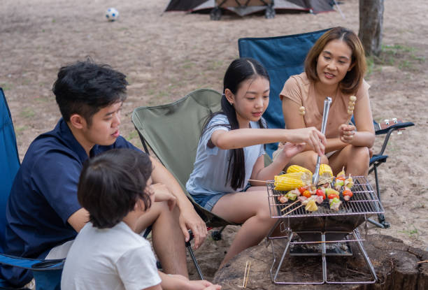 Happy Asian family having barbecue together. Cooking grilled bbq for dinner during camping on summer beach. Happy Asian family having barbecue together. Cooking grilled bbq for dinner during camping on summer beach. family bbq beach stock pictures, royalty-free photos & images