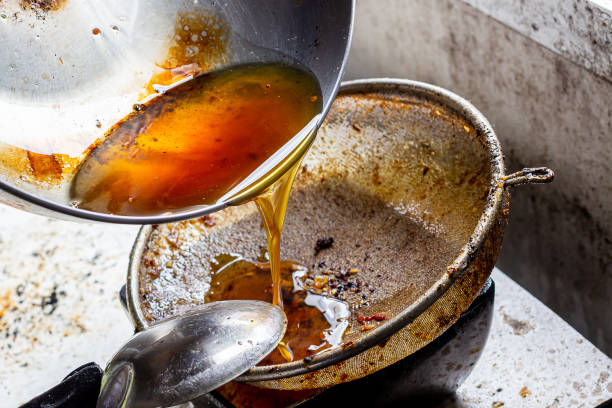 Pouring used cooking oil from frying pan into colander. stock photo