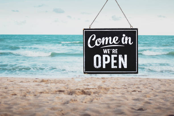 Text on wooden sign "Come in we're open" on the beach stock photo