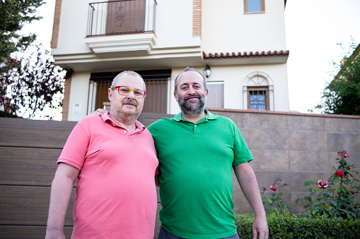Happy middle-aged male couple smiling with their new house. Real estate, LGBT and relationship concept.