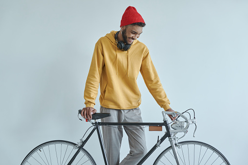 Happy young African man examining his bicycle while standing against the wall