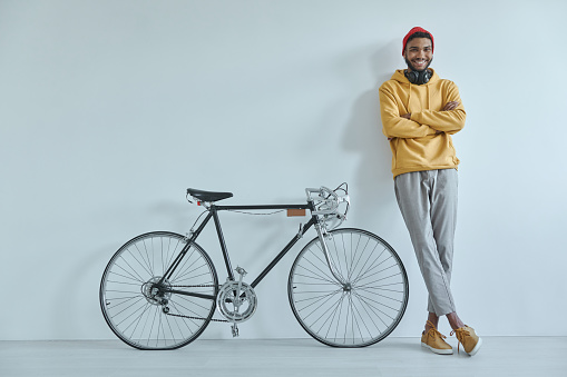 Happy young African man leaning at the wall while standing near his bicycle