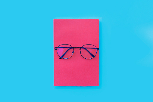Glasses placed on pink book, Placed on blue background, Top view