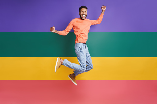Full length of excited African man jumping against colorful background