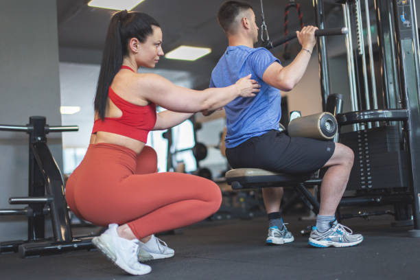 istock Young personal trainer woman helps to client on gym station adjusting back 1406515864