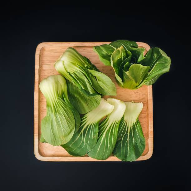 organic green baby bok choy or brassica rapa chinensis on wooden plate on black background. popular chinese vegetable for asian cuisine.healthy vegetarian and vegan eating. - brassica rapa chinensis imagens e fotografias de stock