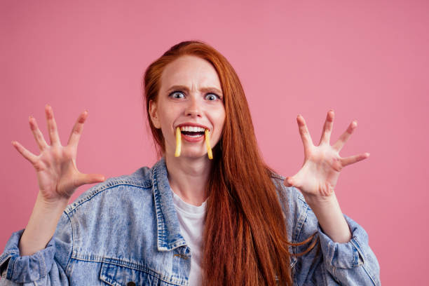 divertente donna di zenzero dai capelli rossi con patate come la paura dei denti canini, le sue mani vogliono afferrarti in studio sfondo rosa. caramelle spaventose o concetto di vita - surprise women humor old fashioned foto e immagini stock