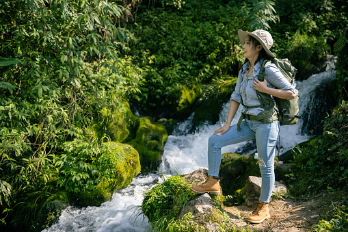 Young woman hikes standing by a stream in a mountain