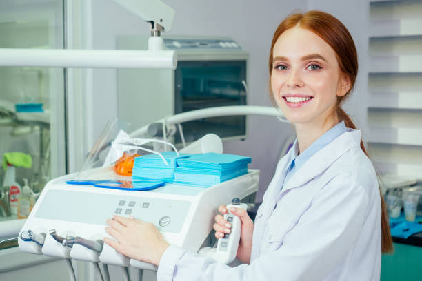 Young beautifu dentist at work in the office . she looking at camera with surgical lamp stock photo