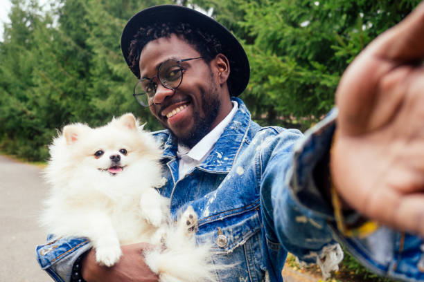 african american man making self portrait with fluffy spitz in summer spring park stock photo