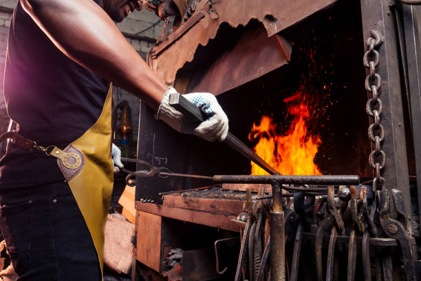 暗いワークショップで炉の隣に鋼を鍛造するハンサムなアフリカのアメリカンマン。中小企業のコンセプト - redhot ストックフォトと画像