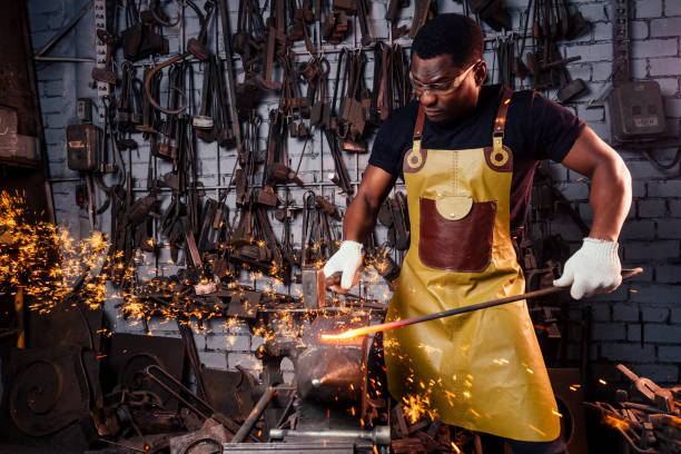 istock handsome african american blacksmith male worker working in workshop,wearing leather apron and protective glasses with gloves.concept save work 1406519685