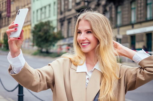 Beautiful rich casual blonde stylish fashion business woman with a phone in her hand make selfie in European buildings and street .
