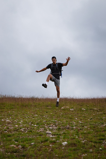Swarthier type of man is running down a gravel hill, checking his every step to avoid injury. Active athlete runs over challenging terrain to improve fitness, coordination and precision of movement.