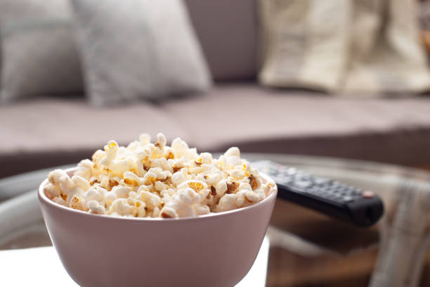 istock Bowl with popcorn and tv remote control on glass table near sofa 1406523458