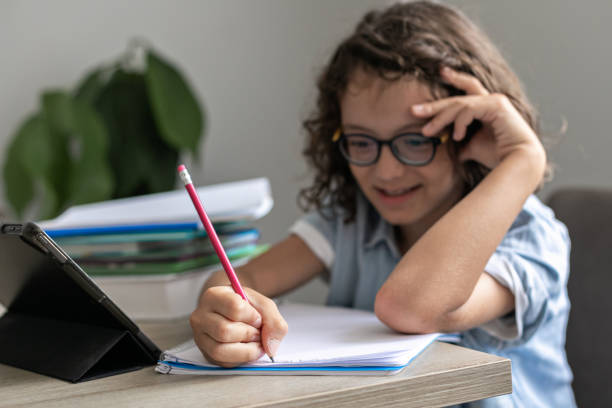 istock Little adorable school boy with eyeglasses, studying online from home. kid using digital tablet 1406529143
