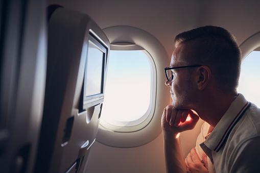 Portrait of man traveling by airplane. Passenger looking through plane window during flight