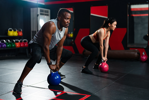 African American man and Asian woman exercising lifting up kettlebell weight in training workout at fitness gym.Strong workout training class.