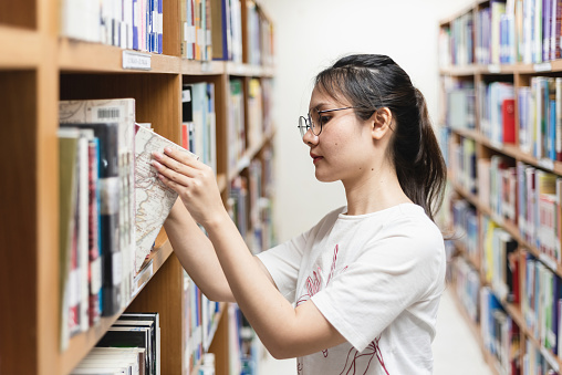 Asian female student browsing book From the shelf in the library.