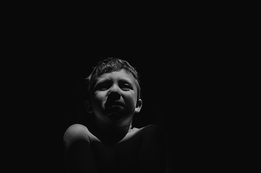 A black and white portrait of sad anonymous little boy