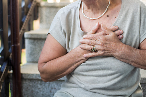 Elderly woman sitting on stairs and holding hands on chest due to short breath. Upset stressed senior woman feeling pain ache touching chest having heart attack, sad worried senior older lady suffers from heartache