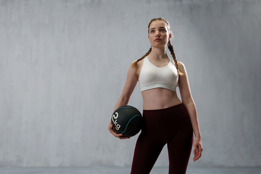 An athletic fitness woman working out with medicine ball on grey background. Copy space.
