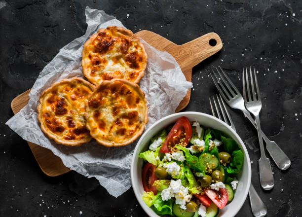 Delicious lunch table - mini canned tuna, mozzarella quiche and fresh Greek salad on a dark background, top view Delicious lunch table - mini canned tuna, mozzarella quiche and fresh Greek salad on a dark background, top view fish pie stock pictures, royalty-free photos & images