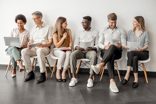 Overjoyed multicultural diverse candidates sit on chairs wait for interview have fun talking, happy multiethnic diverse applicants speak and chat joke laugh before hiring process, employment concept