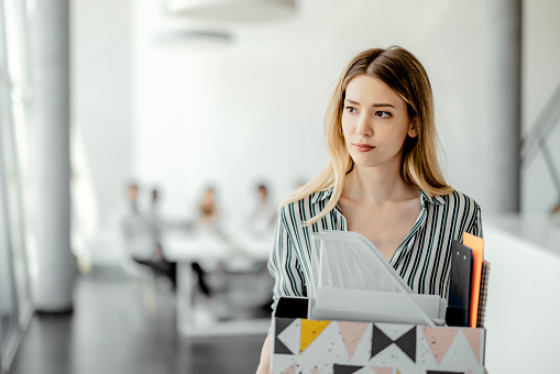 Upset businesswoman with cardboard box of things leaving office after being fired