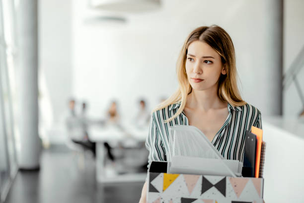 Upset businesswoman being fired Upset businesswoman with cardboard box of things leaving office after being fired resignation stock pictures, royalty-free photos & images