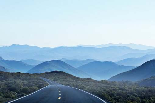 An empty two lane road winds into oblivion toward a series of overlapping mountain ridges of the California  Pacific Coastal Ranges.