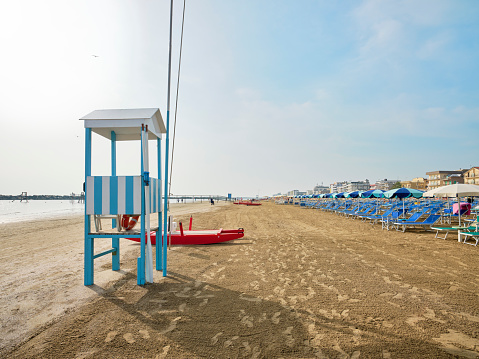 Lifeguard tower next to a lifeboat on the beach on a sunny summer morning, in the background some bathers cooling off on the Adriatic coast, Italy.