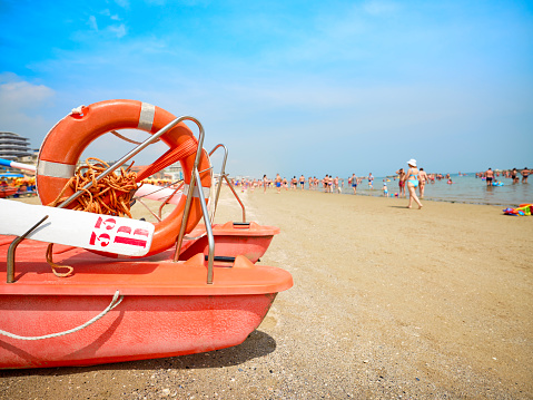 Lifeboat in the foreground on the beach on a sunny summer morning, in the background some bathers cooling off on the Adriatic coast, Italy.