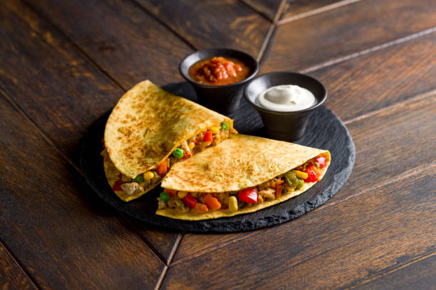 istock Mexican Quesadilla with chicken, vegetables, cheese and sauces on black stone plate 1406554704