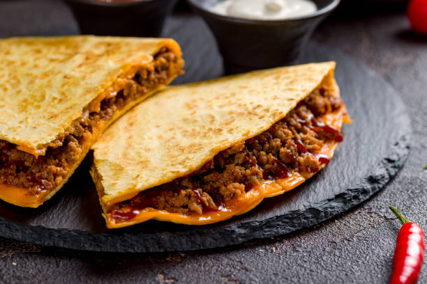 istock Quesadilla with beef, cheese, bbq sauce and sauces on dark stone plate macro close up 1406554777