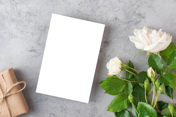 istock Blank greeting card or wedding invitation with white rose flowers and gift box on gray background. Mock up. Flat lay 1406554844