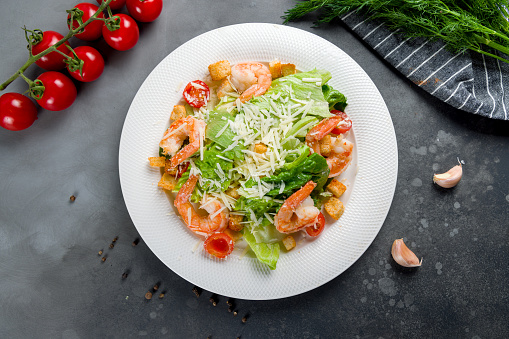 salad caesar with shrimps on white plate top view on grey table