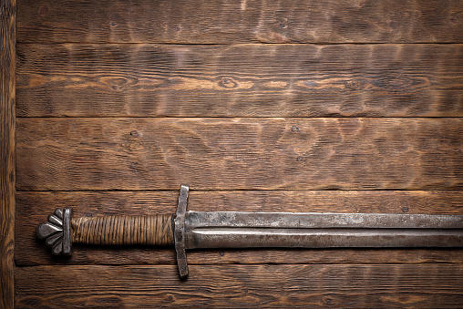 Ancient rusty sword on the wooden table flat lay background with copy space.