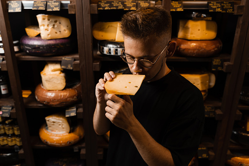 Handsome customer in cheese shop sniff and enjoy limited gouda cheese. Snack tasty piece of cheese for appetizer