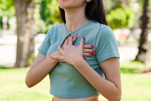 Young beautiful woman wearing turquoise tee on city park, outdoors presses his hands to chest and facial expression pain, having a heart attack. stock photo