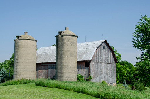 Abandoned silos made of poured cement standing infront of a barn on Wisconsin farm. Near Cambria, Wisconsin, USA.