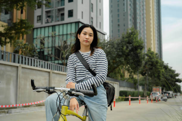 Attractive Asian creative riding bicycle through business district in the morning, enjoying sustainable lifestyle.