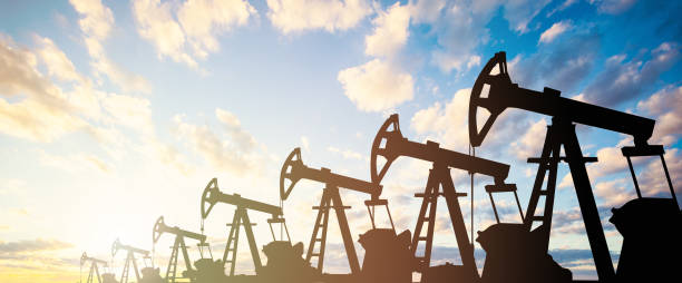 Oil pump jack. Oil industry equipment silhouette against blue sky clouds background Oil pump jack. Oil industry equipment silhouette against blue sky clouds background oil field stock pictures, royalty-free photos & images
