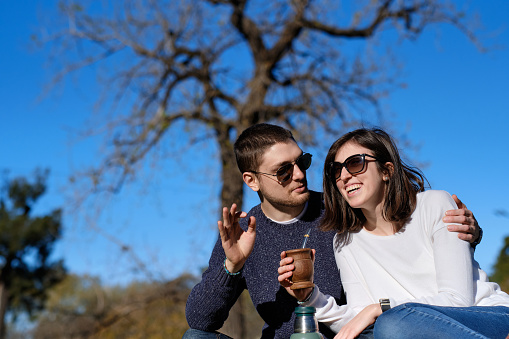 Couple enjoying in a park drinking mate a South American cultural drink.