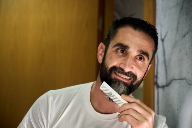 Young man grooming and combing his beard with comb in front of mirror. High quality photo